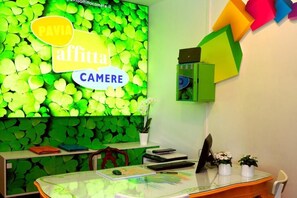 A room with a green leaf-patterned wall, a glass table, and a desk with a computer and office supplies. - Pavia AffittaCamere (Pavia)
