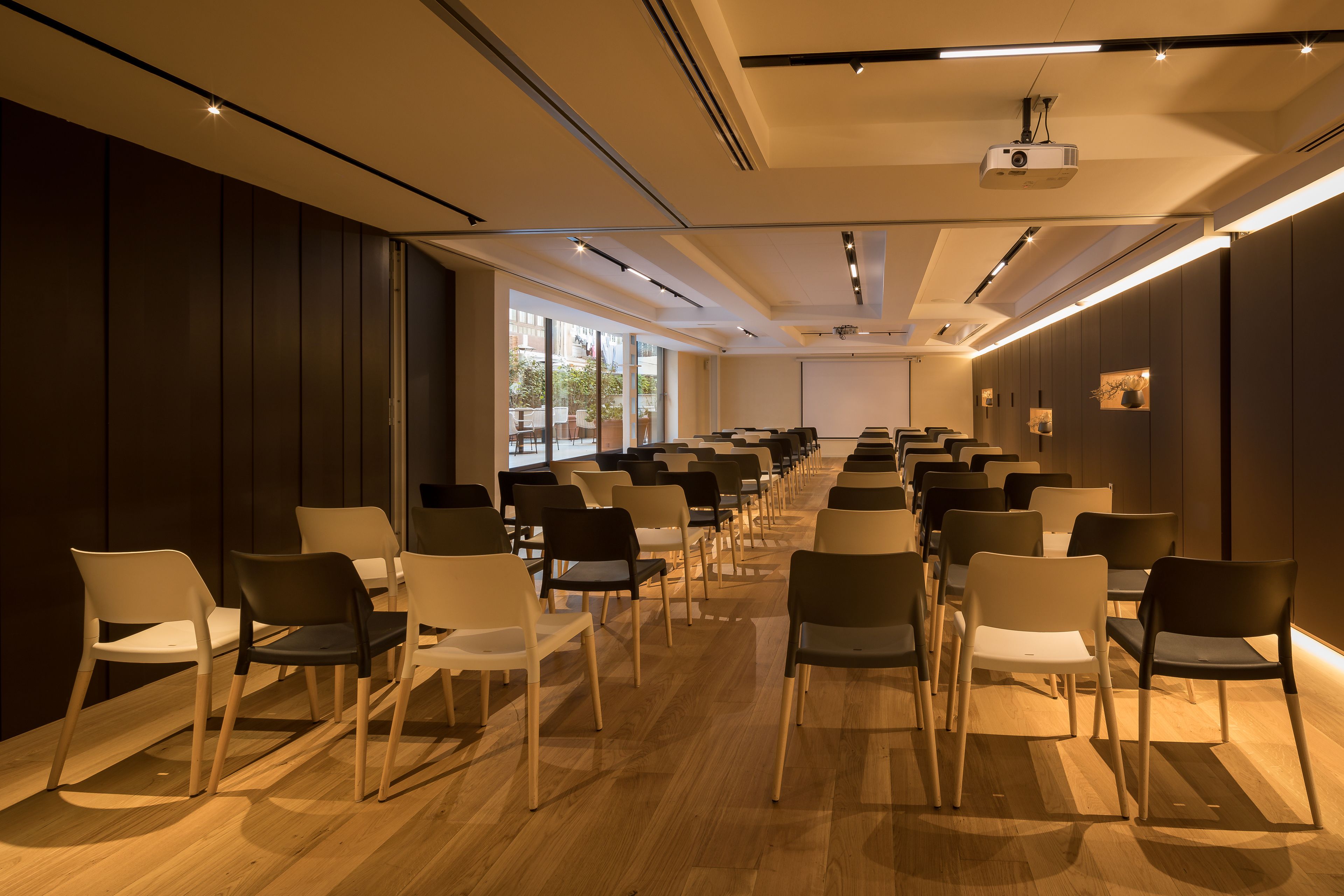 A conference room with rows of chairs, a projector, and a large window providing natural light.