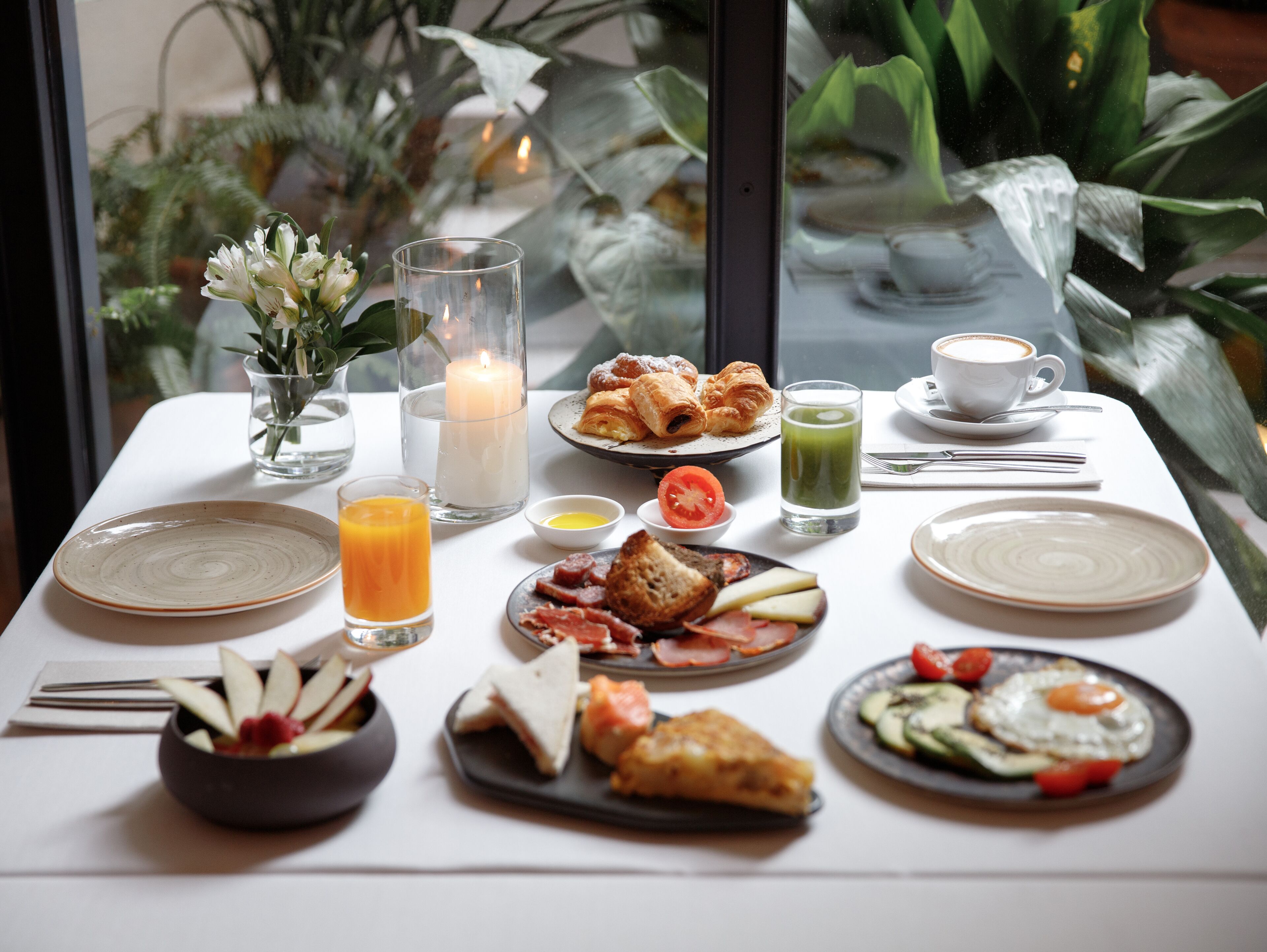 A breakfast table with various dishes, a candle, and a cup of coffee.