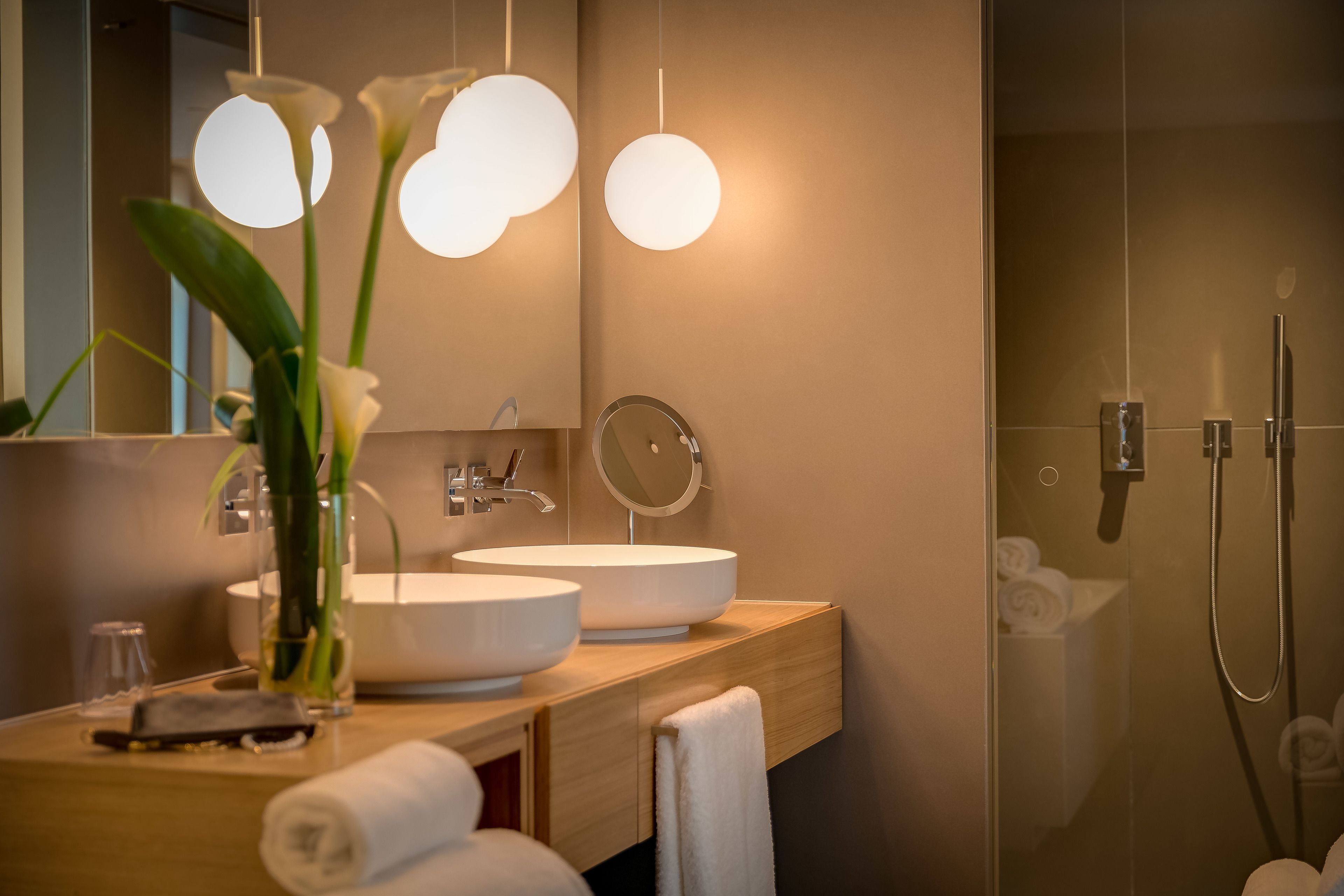 A modern bathroom with two round white sinks, a mirror, and a glass-enclosed shower.