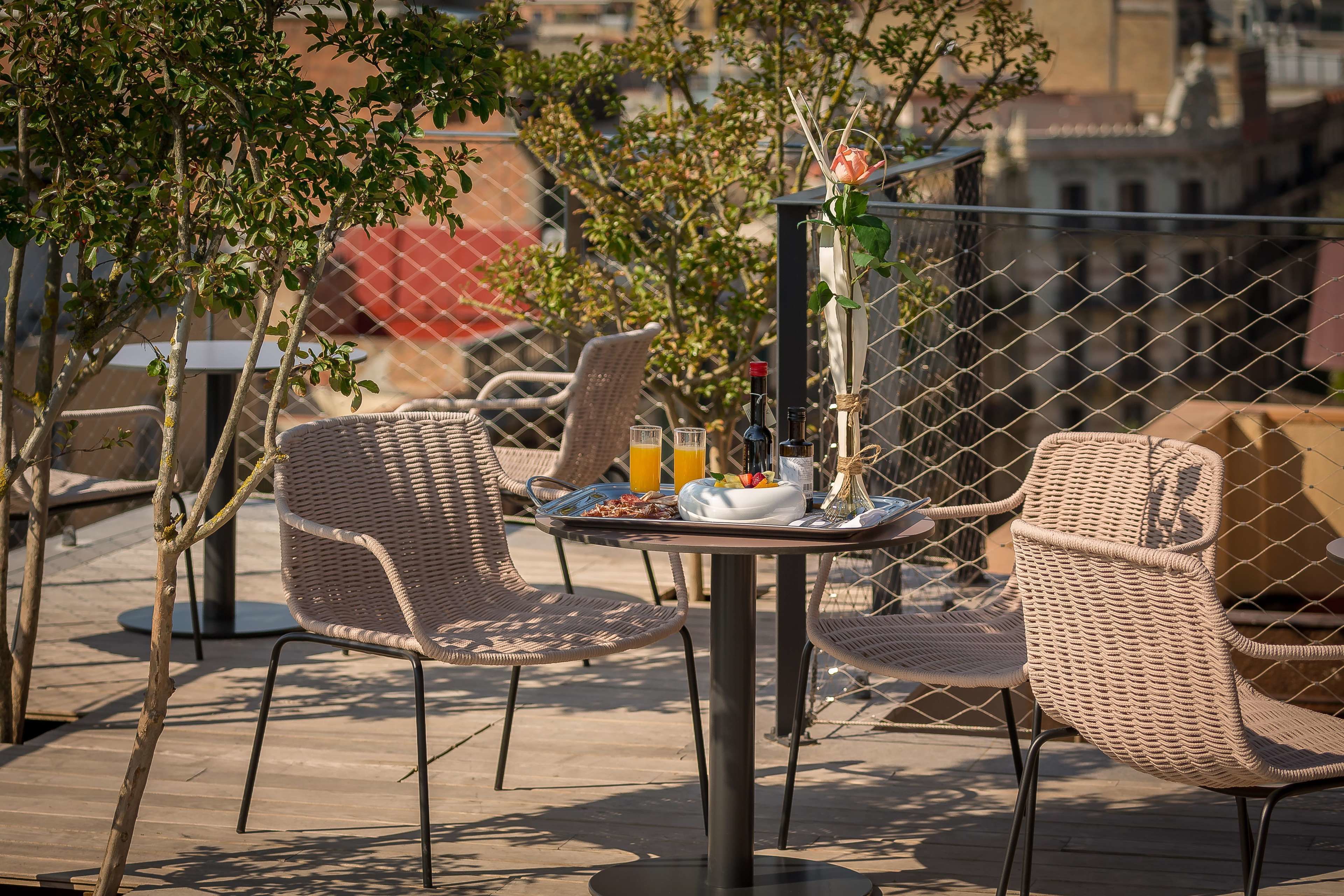A rooftop terrace with wicker chairs, a table with breakfast items, and a city view.