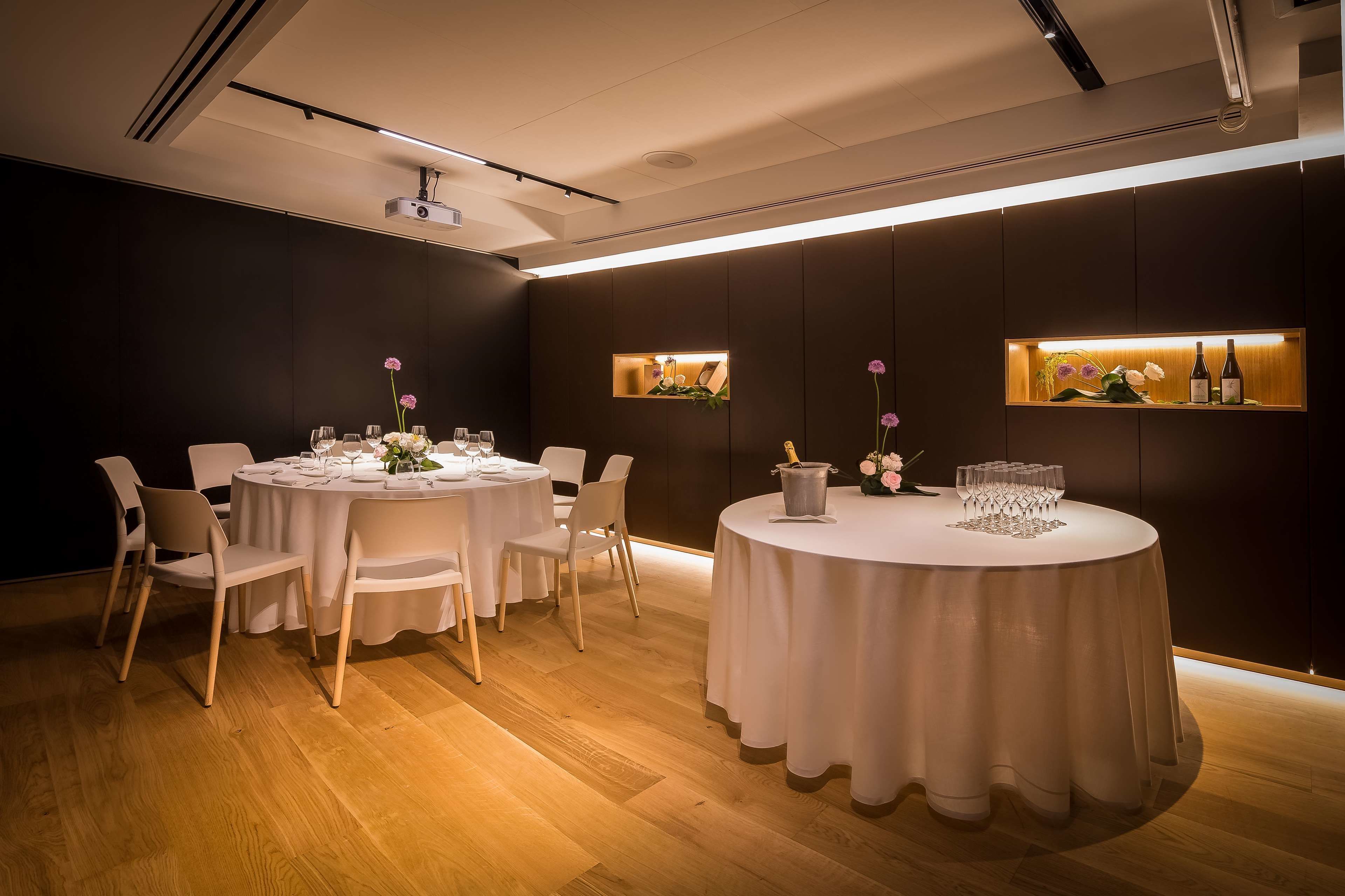Un comedor moderno con mesas redondas, sillas blancas y suelo de madera.