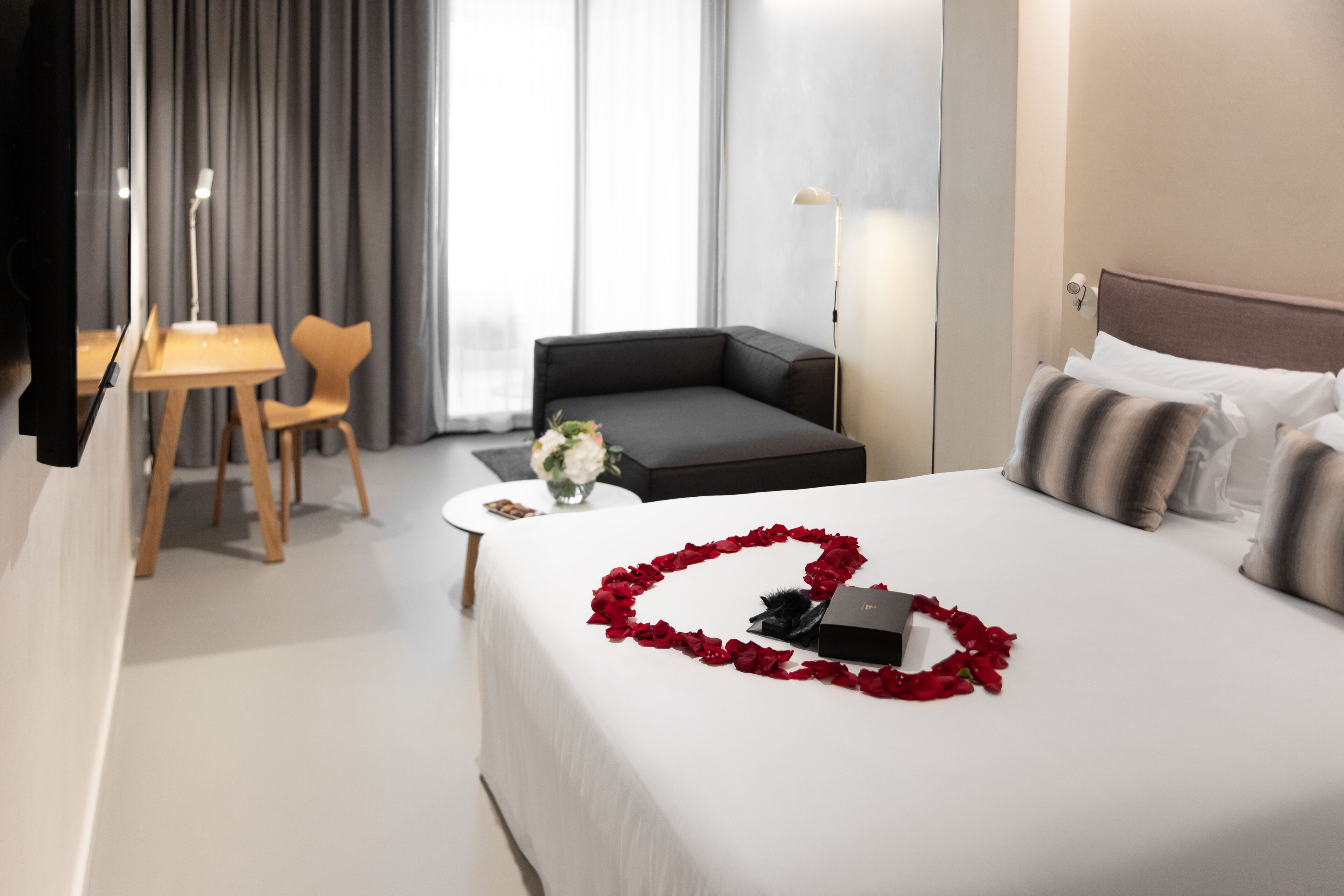 Een hotelkamer met een opgemaakt bed, een bank, een kleine tafel met een bloevas en een bureau met een stoel.