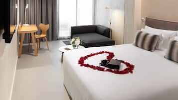 Een hotelkamer met een opgemaakt bed, een bank, een kleine tafel met een bloevas en een bureau met een stoel.