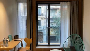 A room with a wooden table, two chairs, a small round table, and a green chair by a large window with curtains.