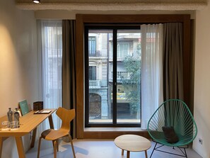A room with a wooden table, two chairs, a small round table, and a green chair by a large window with curtains.