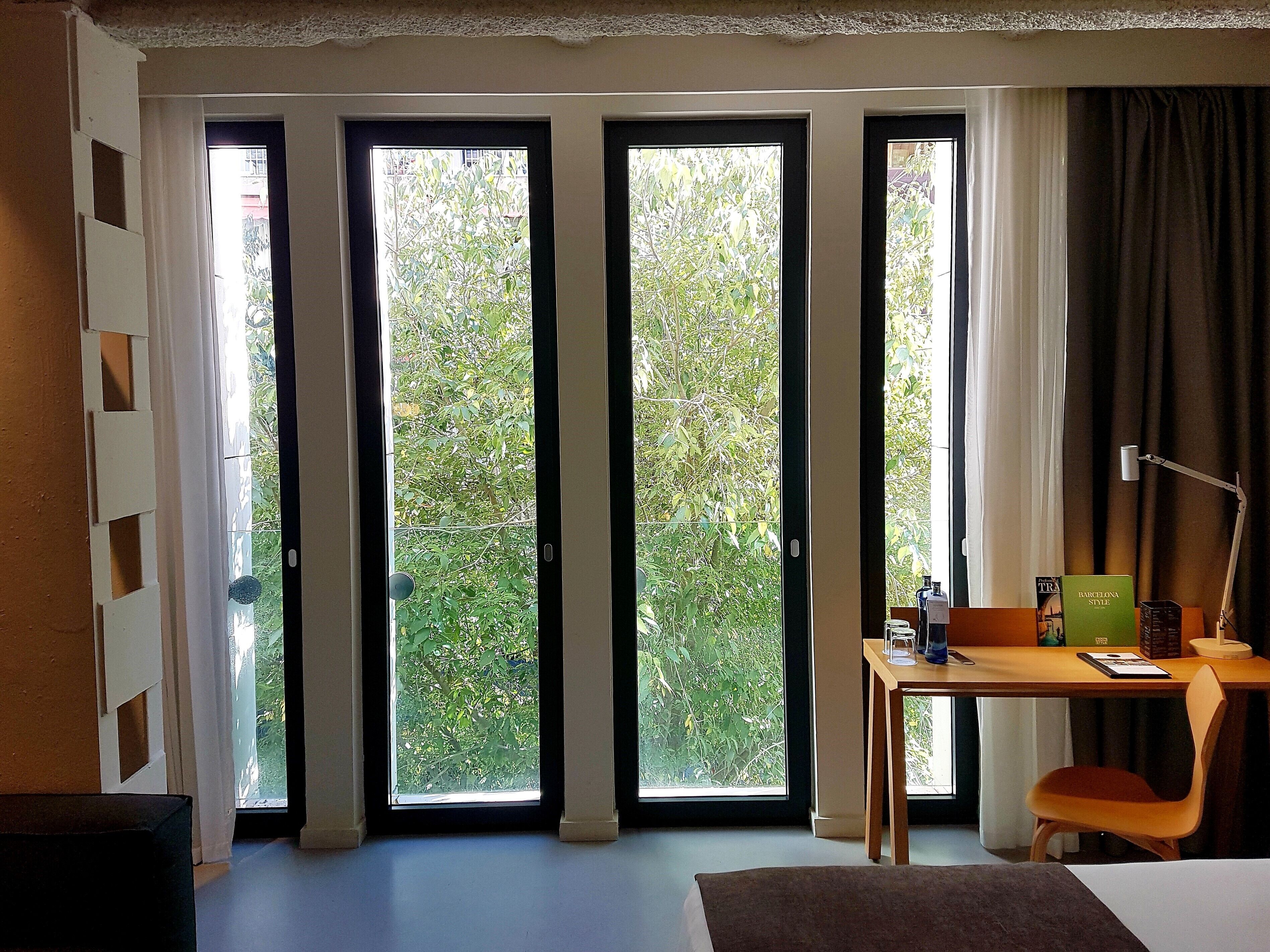 Una habitación de hotel con ventanas amplias, un escritorio, una silla y una cama.