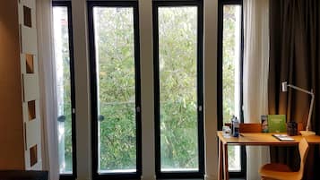 Una habitación de hotel con ventanas amplias, un escritorio, una silla y una cama.