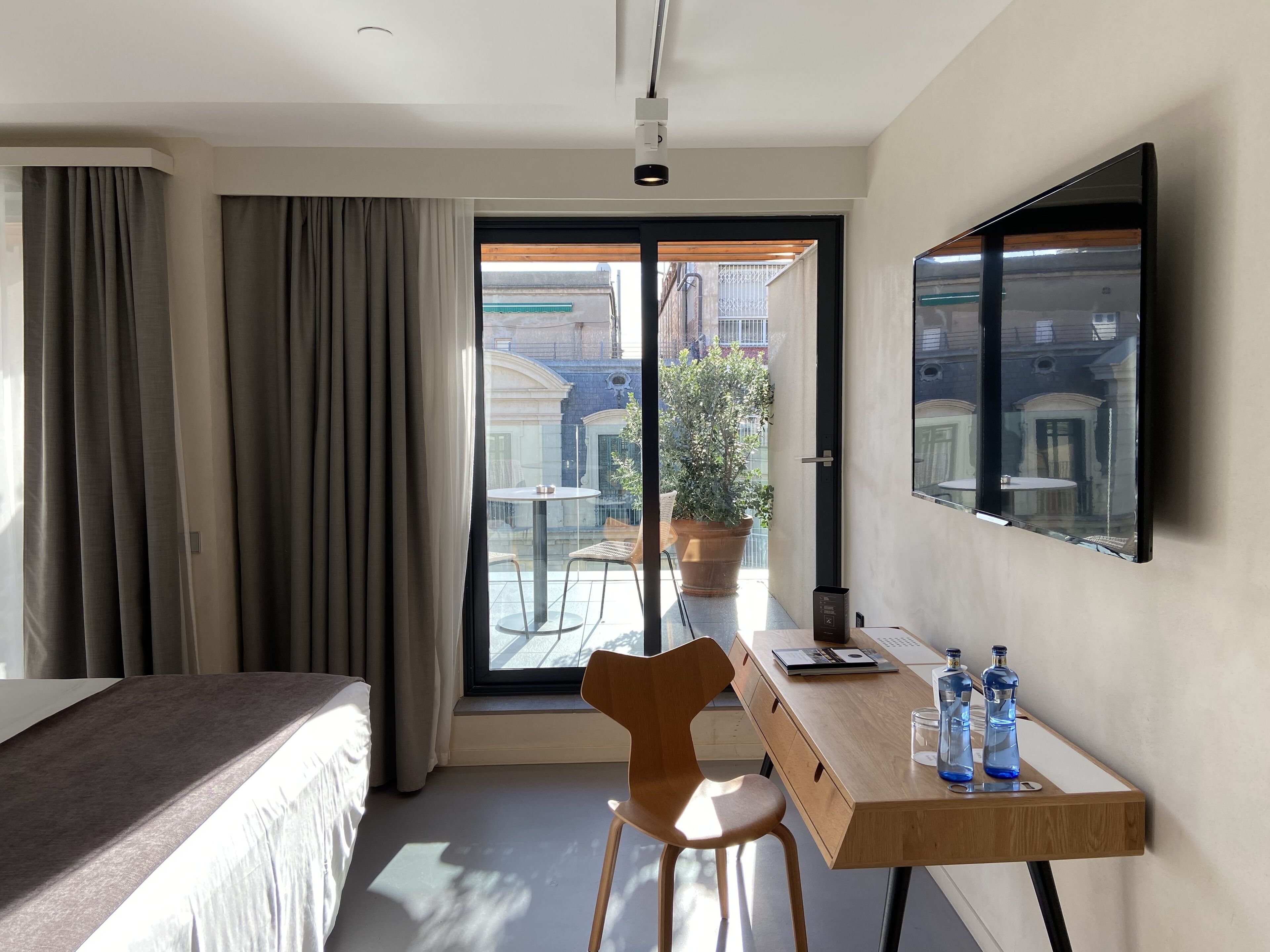 Hotelkamer met een bed, een bureau met stoel, een potplant en uitzicht op het buitenbalkon.