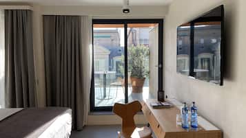 Hotelkamer met een bed, een bureau met stoel, een potplant en uitzicht op het buitenbalkon.