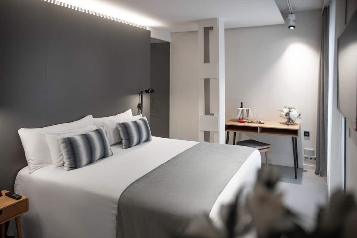 A modern hotel room with a large bed, bedside tables, a desk, and a chair.
