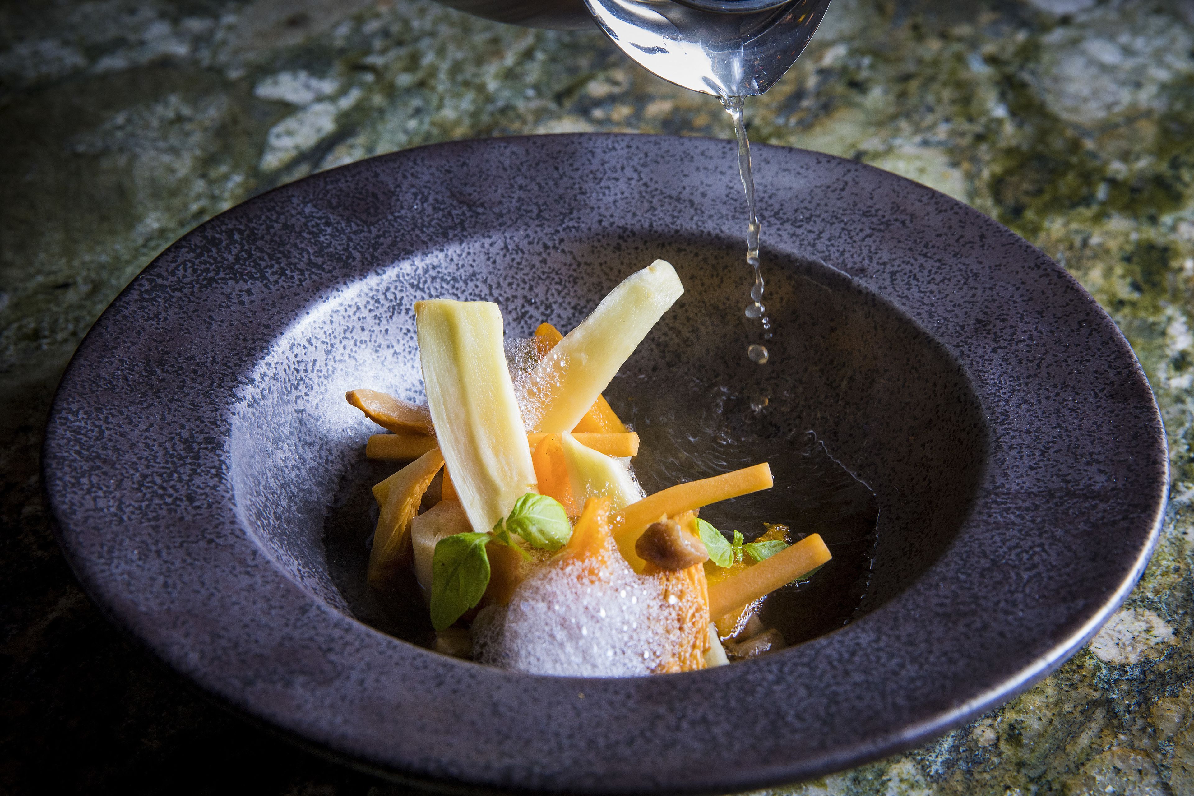 A bowl of food with various ingredients and a liquid being poured over it.