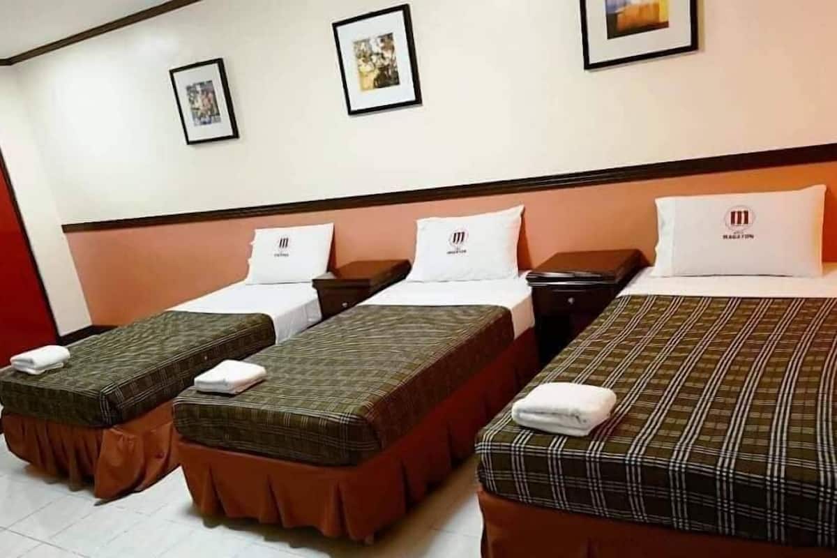 A hotel room with three single beds, each with a pillow and a folded towel. There are framed pictures on the wall above the beds.