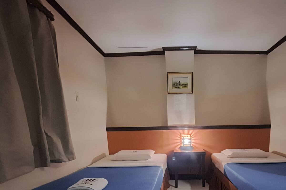 A hotel room with two single beds, a nightstand, a wall-mounted picture, and a window with curtains.
