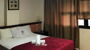 A hotel room with a bed, a nightstand, a lamp, and a window with curtains. - Magayon Hotel (Legazpi)