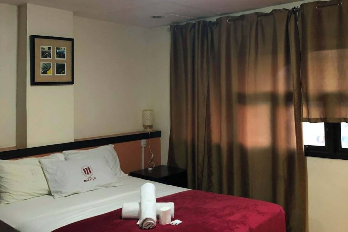 A hotel room with a bed, a nightstand, a lamp, and a window with curtains.