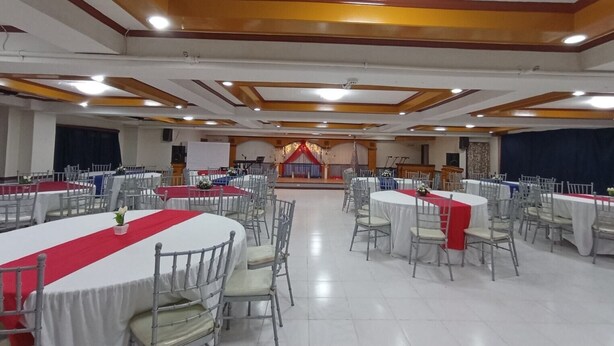 A banquet hall with round tables covered in white tablecloths and red runners, arranged in rows. - Magayon Hotel (Legazpi)