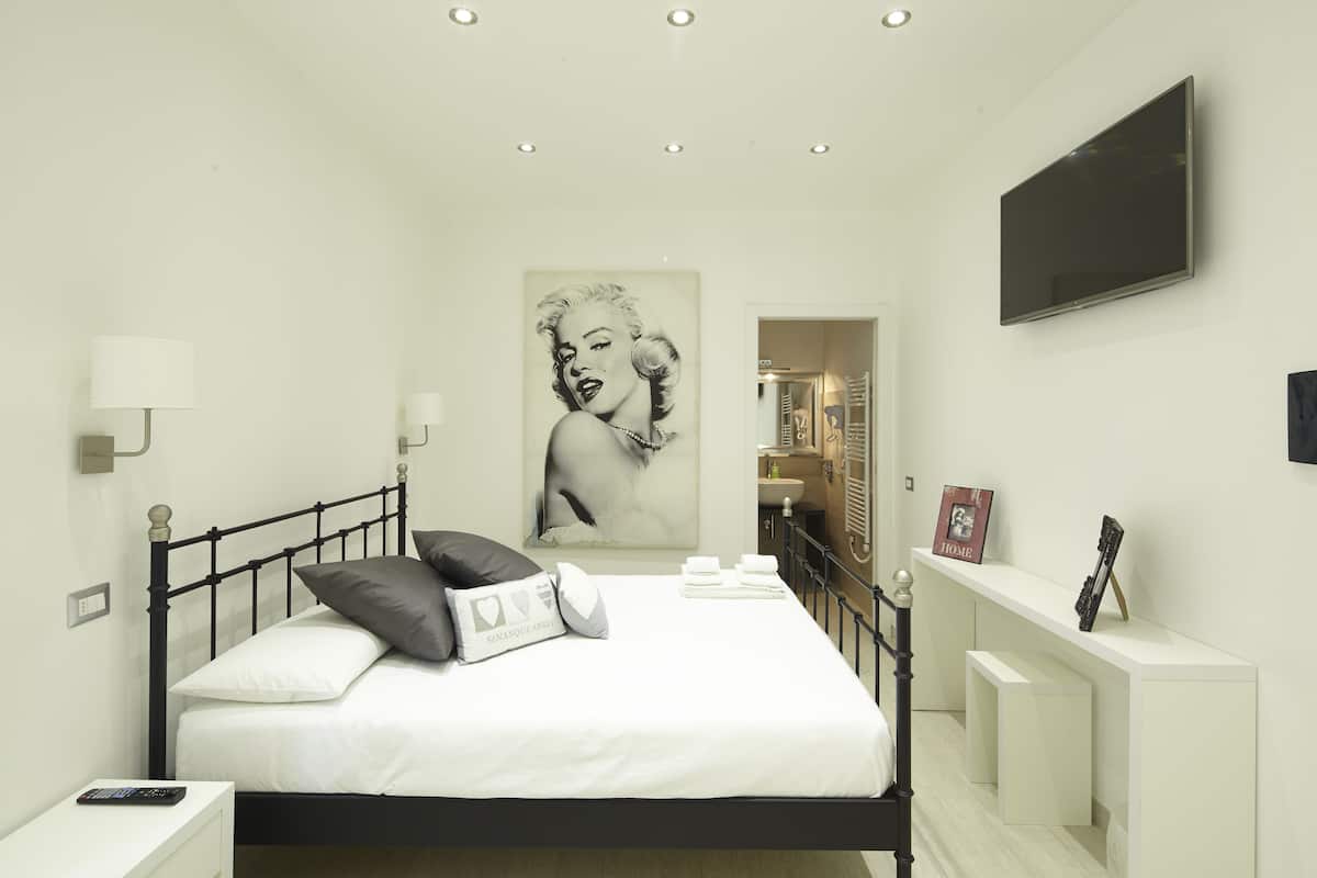 A modern bedroom with a bed, bedside tables, a wall-mounted TV, and a large portrait.