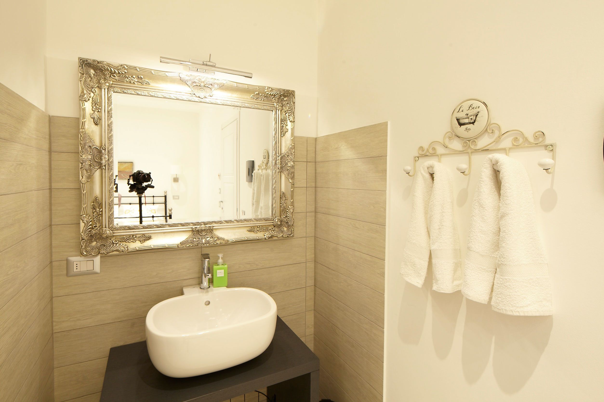A bathroom with a large ornate mirror, a white sink, and a towel rack with white towels.
