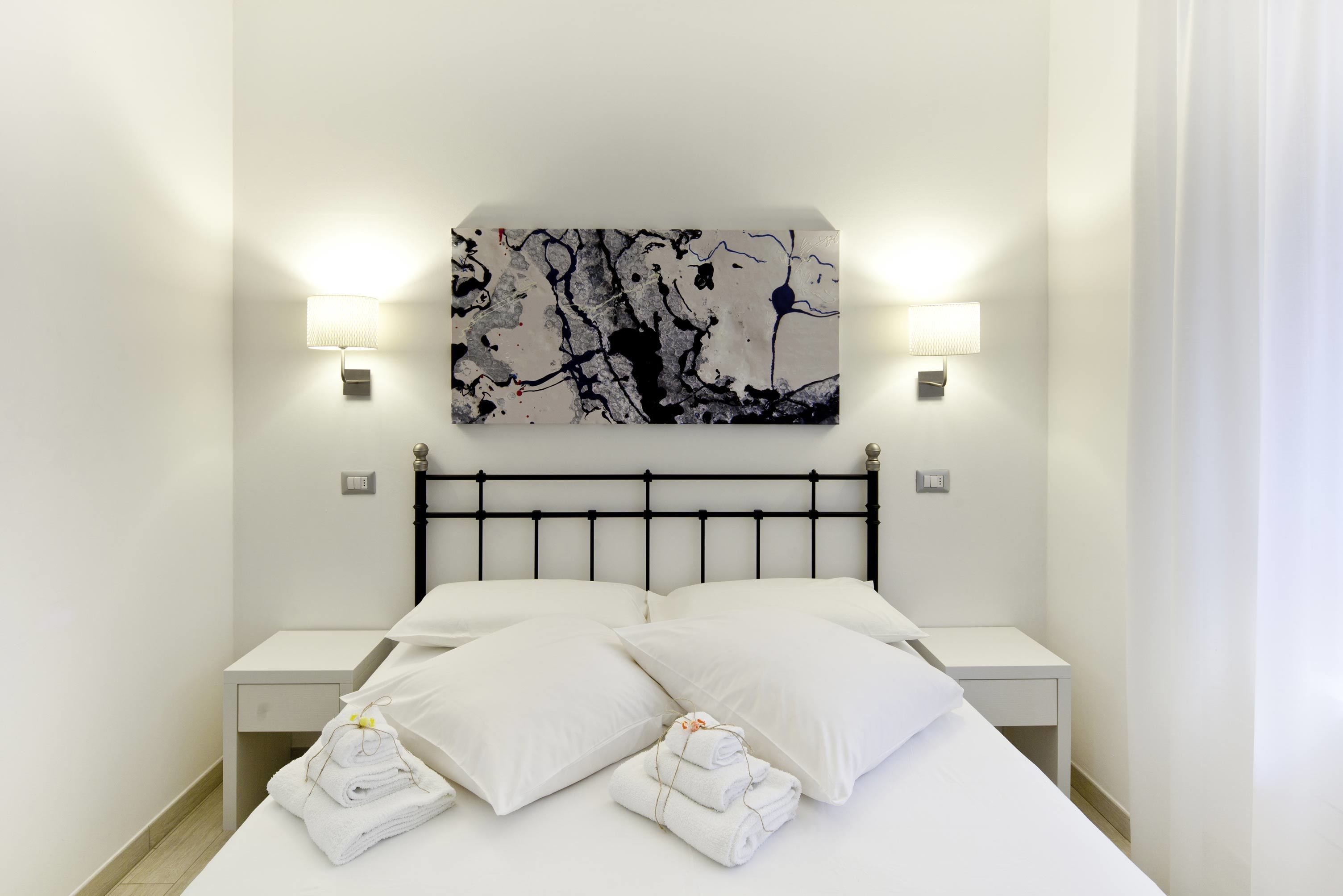 A modern hotel room with a bed, two bedside tables, and a large abstract painting on the wall.