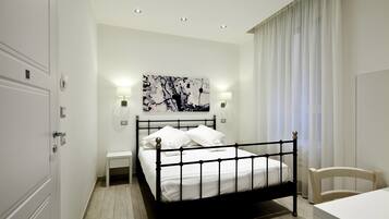 A modern bedroom with a black metal bed frame, white bedding, a bedside table with a lamp, and a large abstract painting on the wall.
