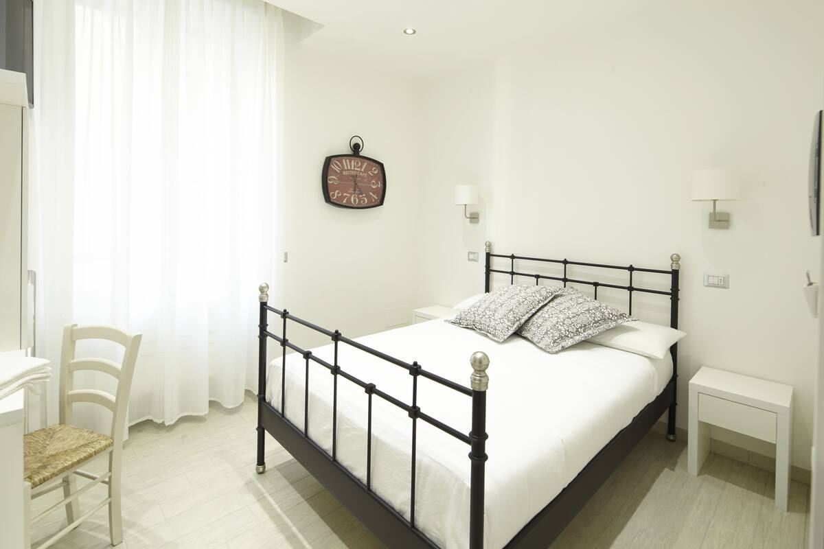 A neatly arranged bedroom with a bed, bedside tables, a chair, and a wall clock.