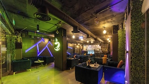 Et moderne loungeområde med siddepladser og bar, med synlige ventilationsrør og grøn vægdekoration.