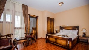 Una habitación de hotel con una cama de madera, un escritorio, una silla y un ventanal con cortinas.