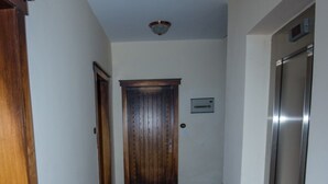 Un pasillo con una puerta de madera, un ascensor metálico e un portero automático en la pared.