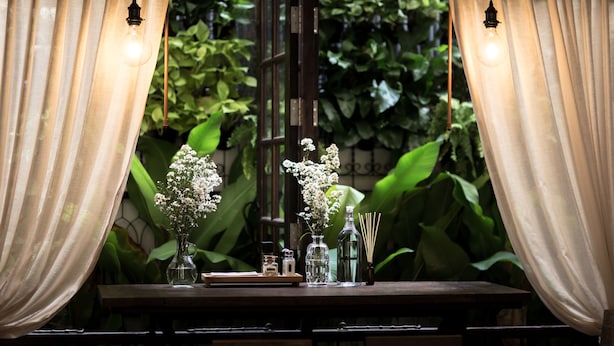 A table with a vase of flowers, a glass bottle, and a small container, set against a window with curtains. - ONCE (upon a time) Chiang Mai Boutique Home (Chiang Mai)