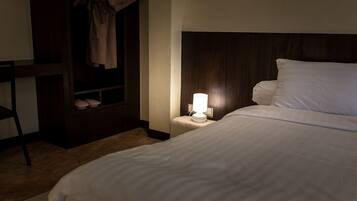 A hotel room with a bed, a bedside table with a lamp, a wardrobe, and a shelf with toiletries.