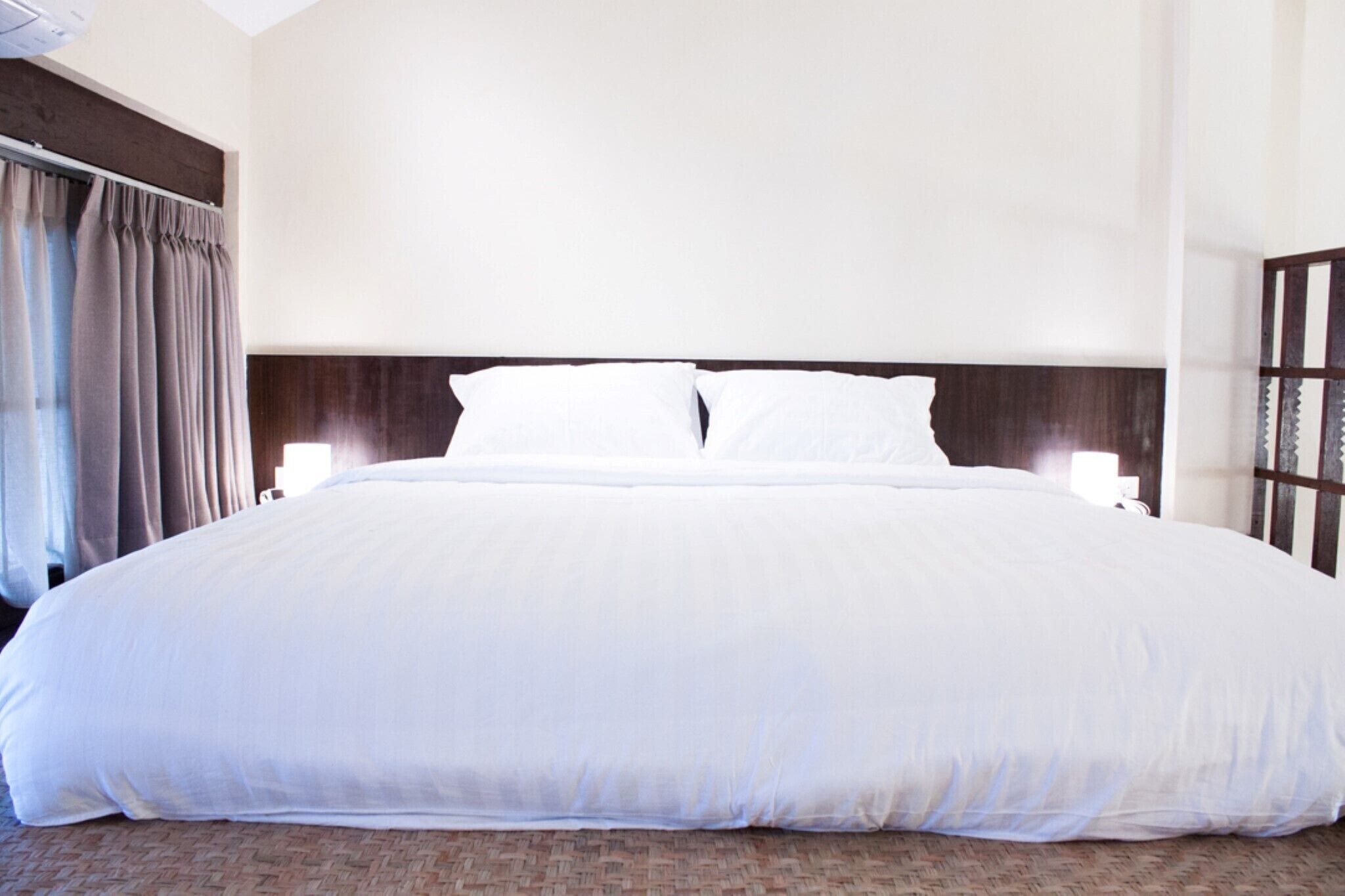 Una cama grande con sábanas blancas, cabecera de madera y dos lámparas de noche.