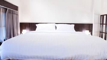 Una cama grande con sábanas blancas, cabecera de madera y dos lámparas de noche.