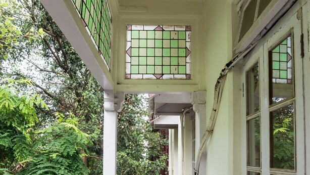A narrow corridor with a checkered floor, white railing, and green-tinted windows. - Bentleys Hotel Colaba (Mumbai)