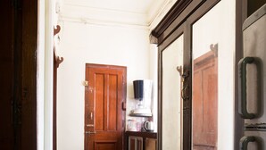 A narrow hallway with a checkered floor, wooden doors, and a cabinet with drawers. - Bentleys Hotel Colaba (Mumbai)