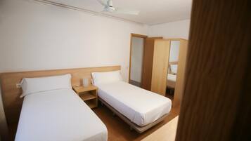 Habitació d'hotel amb dos llits individuals, un capçal de llit de fusta, una taula de nit, un ventilador de sostre i un armari.