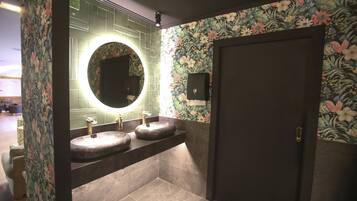 Un baño con dos lavabos, un espejo redondo y papel tapiz con motivos florales.