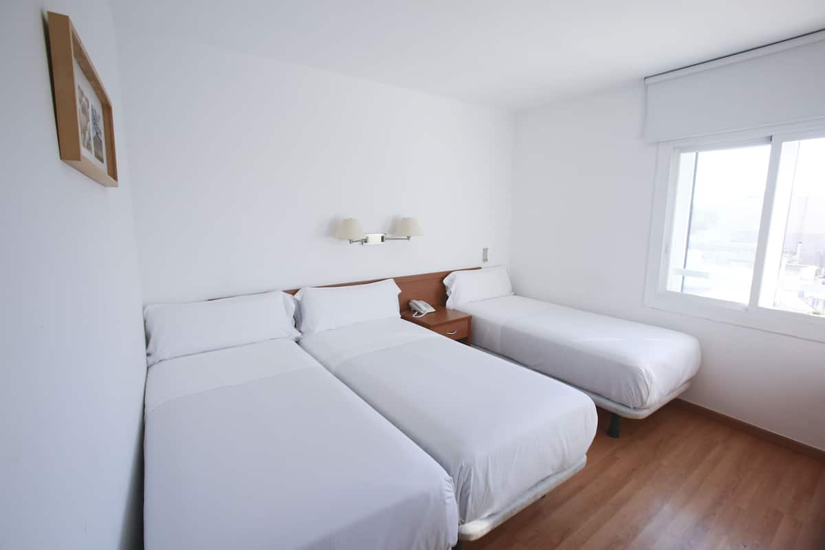 Een hotelkamer met twee eenpersoonsbedden, een nachtkastje met een telefoon, en een raam met jaloezieën.
