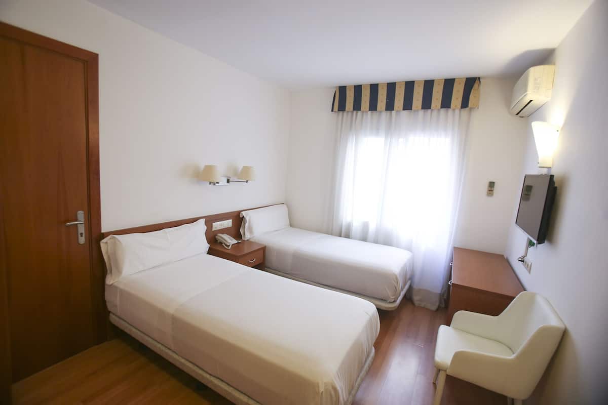 Een hotelkamer met twee bedden, een bureau, een stoel, een televisie en een raam met gordijnen.