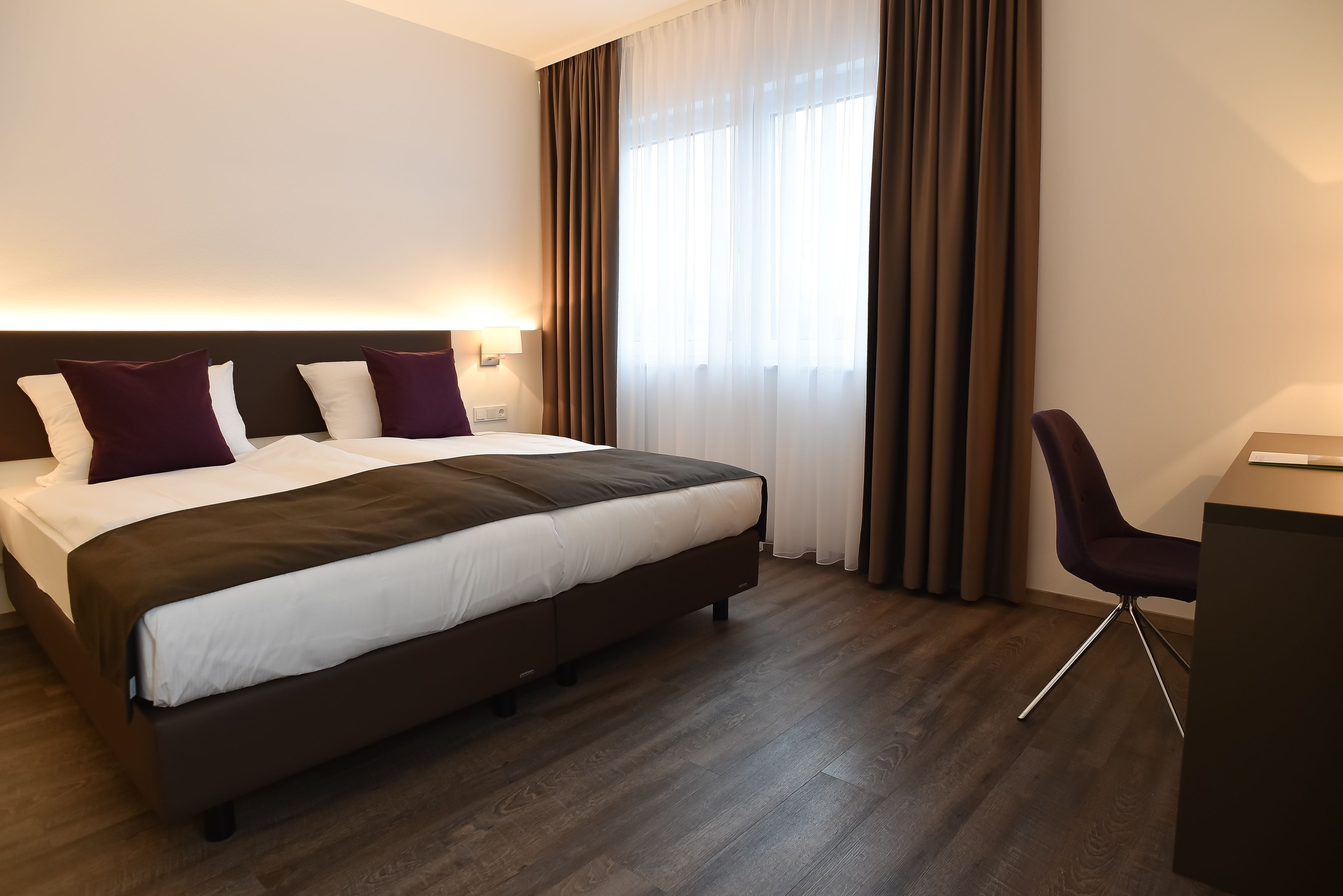 A hotel room with a large bed, a desk, and a chair.