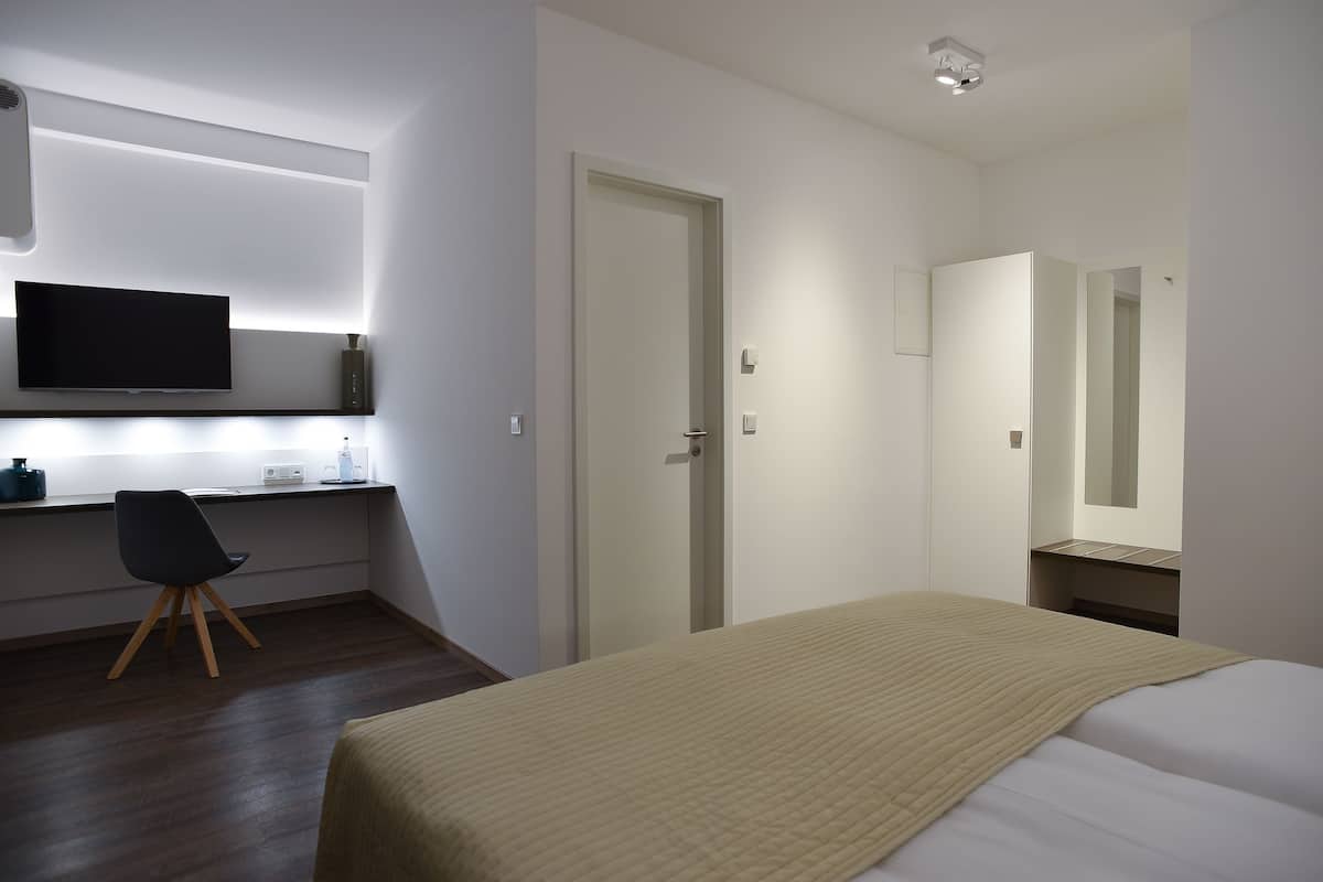 A hotel room with a bed, a desk with a chair, a television, and a mirror.