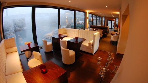 A modern interior with a large window, a seating area with a sofa and chairs, a wooden table, and a chandelier. - Guesthouse Lichtenau (Nussloch)