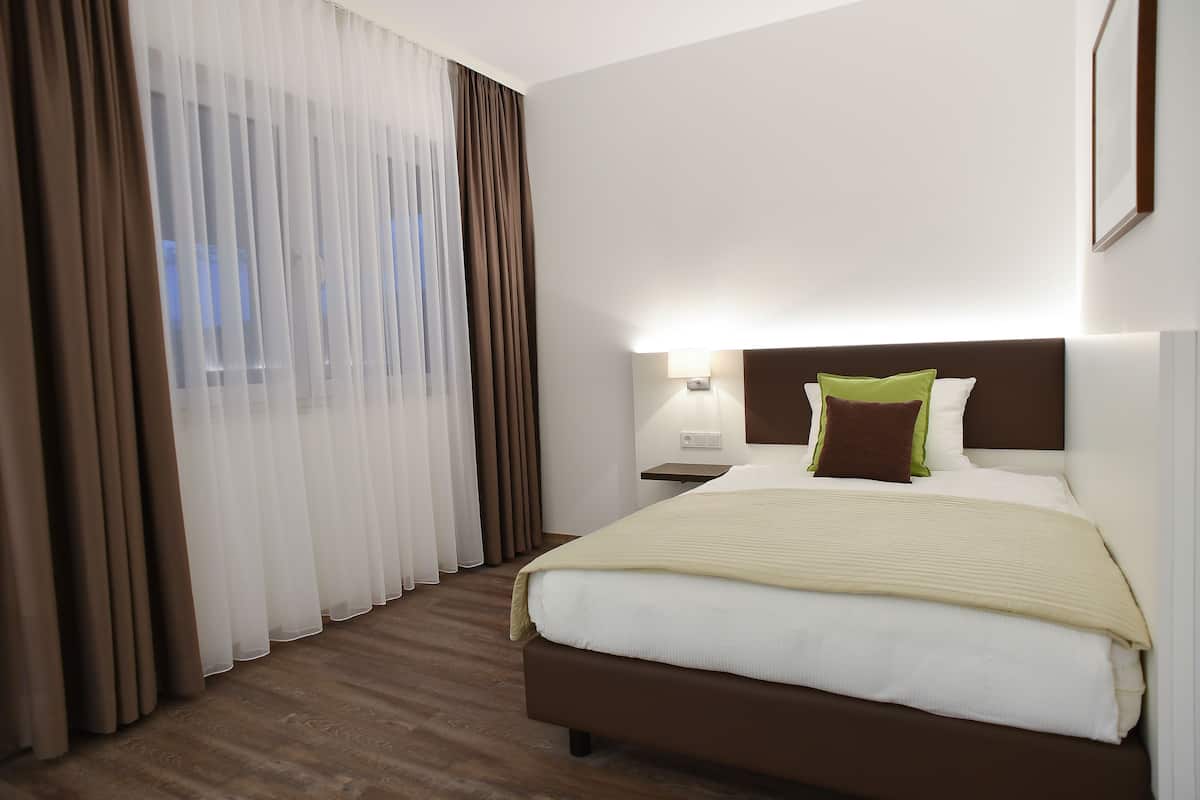A hotel room with a large bed, a nightstand, a lamp, and sheer curtains.