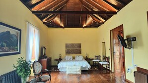 A spacious room with a high wooden ceiling, a large bed with a white bedspread, a wooden floor, and a dining area with a table and chairs. - Casa Rural El Borbullón (Teror)