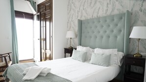 Una cama bien hecha con sábanas blancas y un plaid verde, un cabecero capitonado y dos lámparas de noche sobre mesitas oscuras.