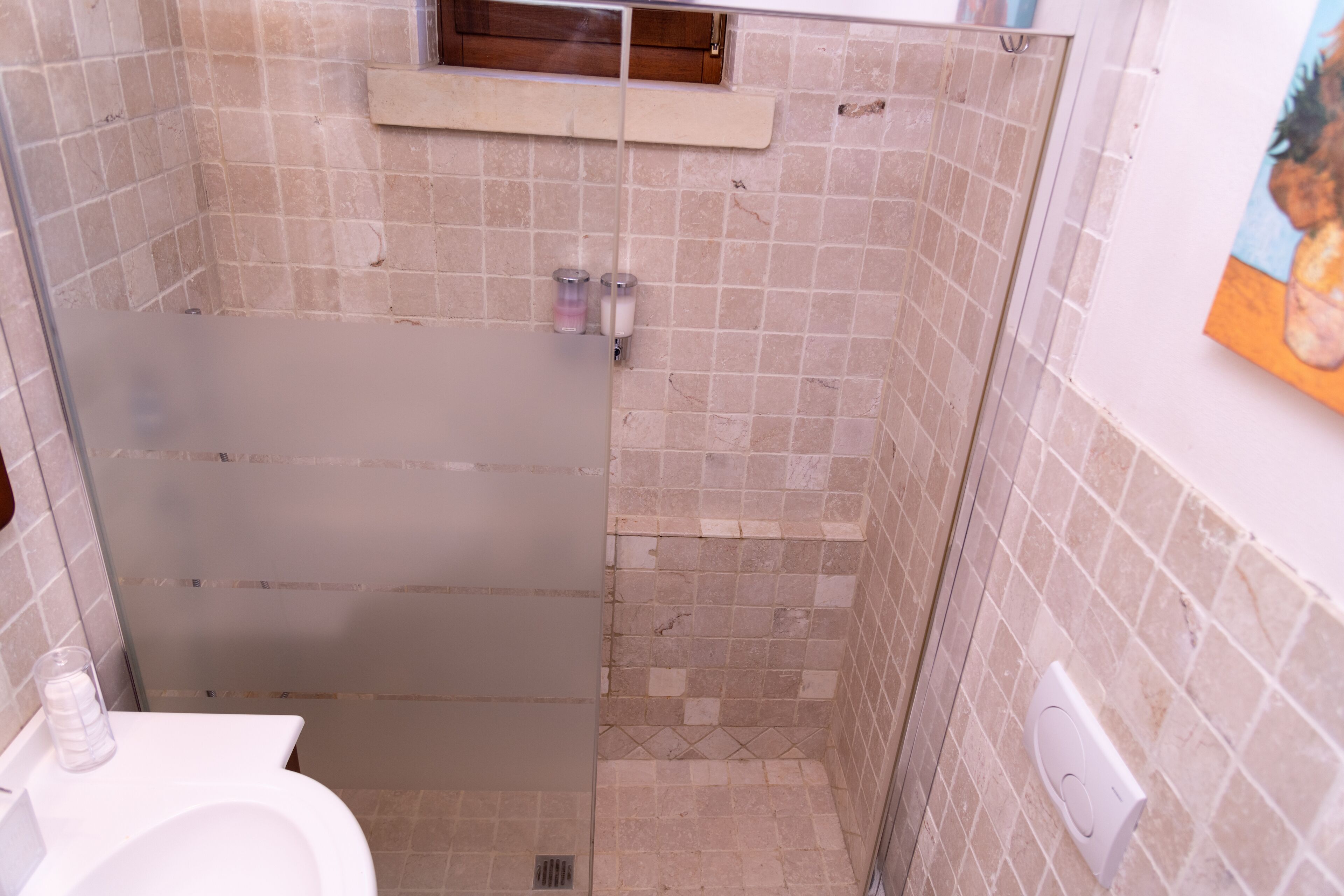 A bathroom with a shower, toilet, and a small shelf with toiletries.