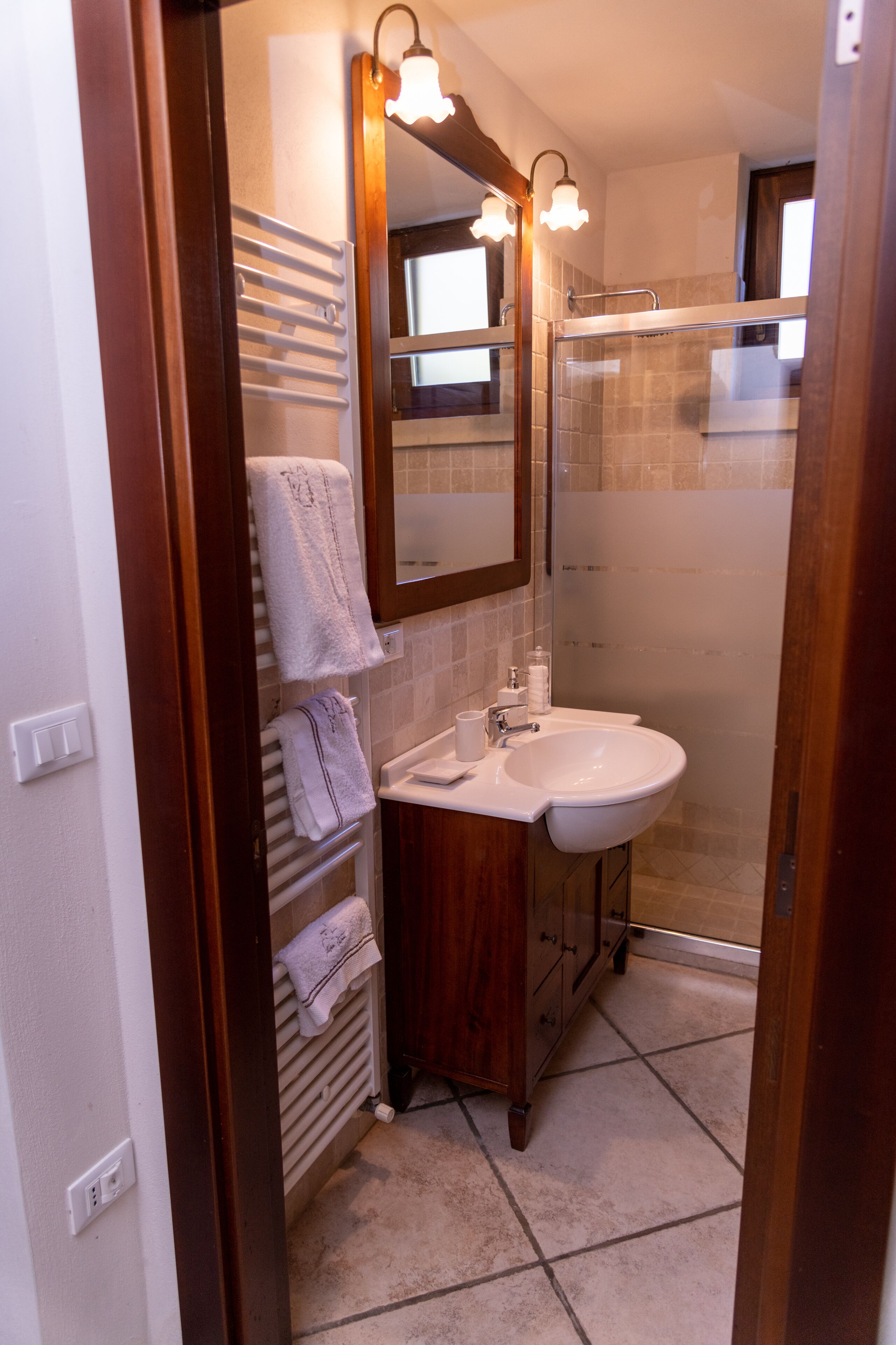 Un baño con lavamanos blanco, mueble de madera, toallero y cabina de ducha de cristal.