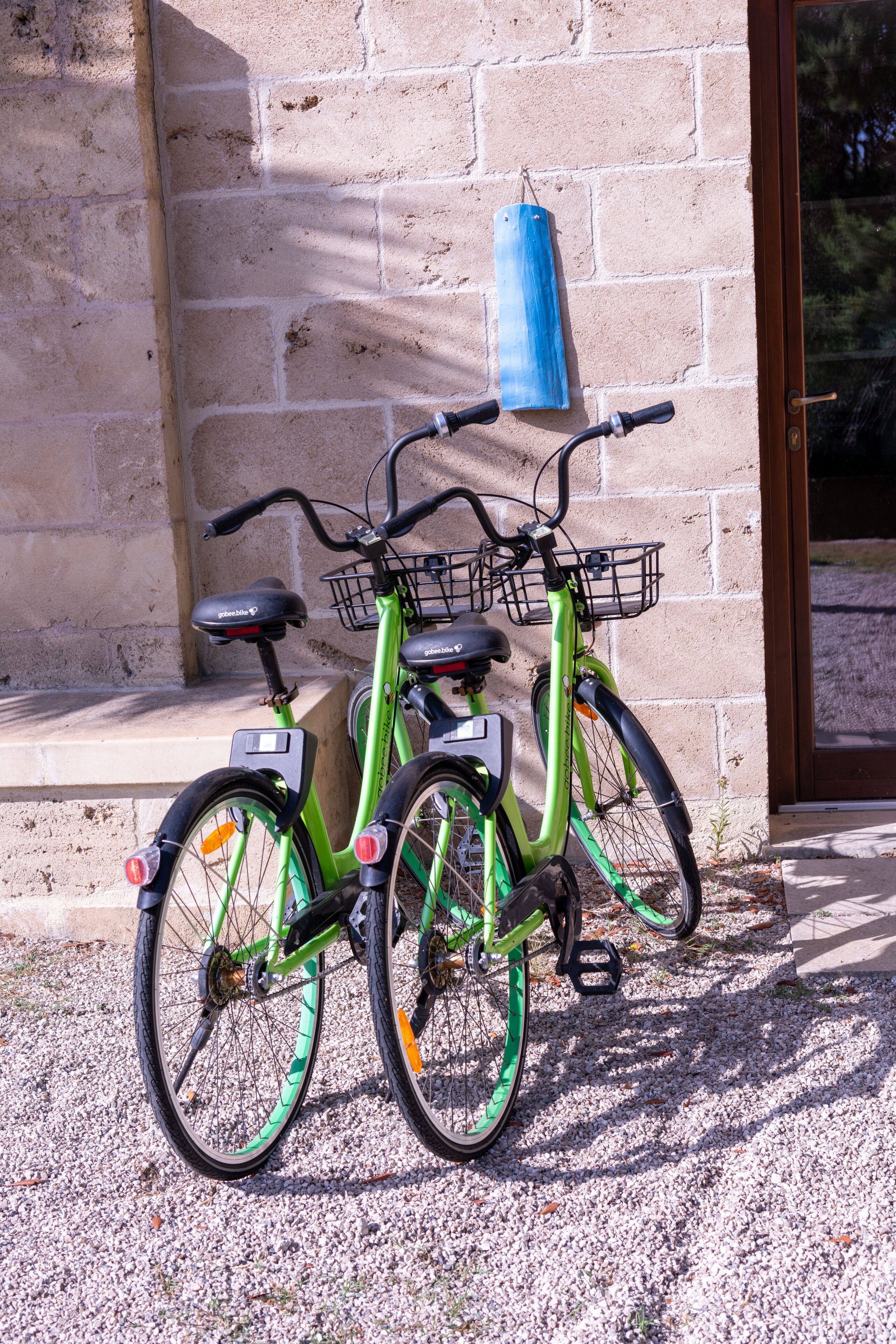 Two green bicycles parked against a brick wall with a blue object hanging on it.