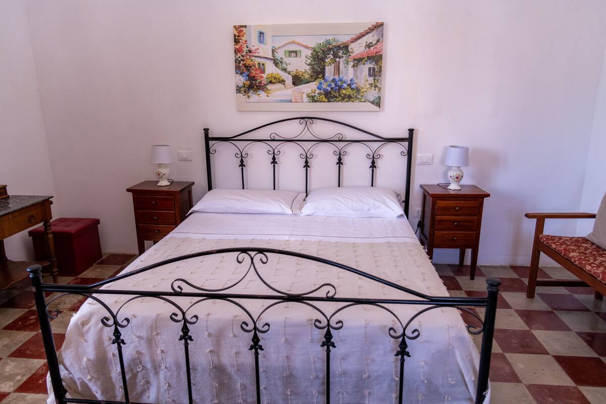 A bedroom with a bed, two bedside tables, a chair, a dresser, and a painting on the wall.