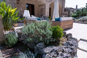 Un edificio de piedra con mobiliario exterior, incluyendo un sofá y sillones de mimbre, rodeado de plantas y rocas.